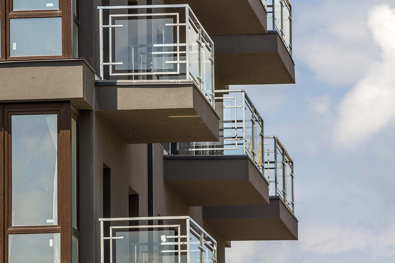 Close-up detail of new apartment building wall with balconies and shiny windows on blue summer sky copy space background. Modern architecture, comfortable home, professional building concept.